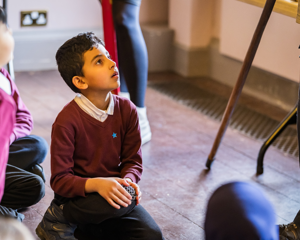 young male school kid sat on the floor listening to a historian
